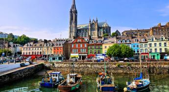 Photo of boats on a river near colorful buildings and a church.