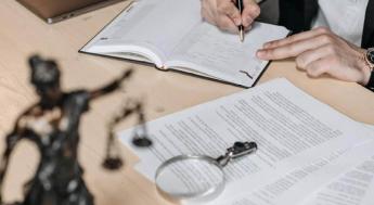 Photo of documents and magnifying glass with person writing in pen.