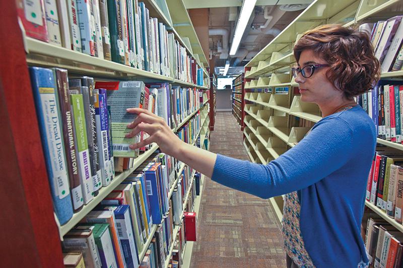Student pulling a book from a library book stack.